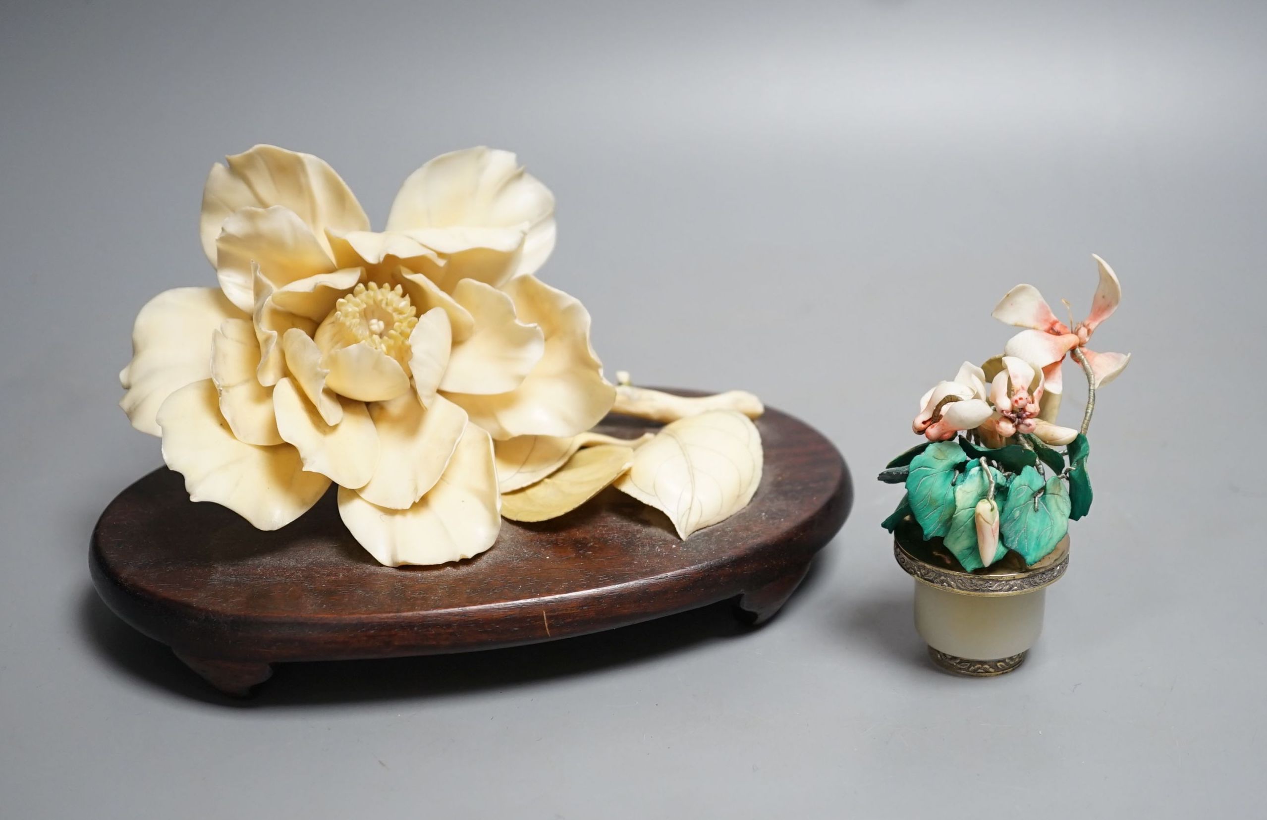 A Chinese ivory model of a peony flower on stand and a Chinese coloured ivory model of flowers with a white jade and white metal plant pot, first half 20th century. Largest measurement 19cm